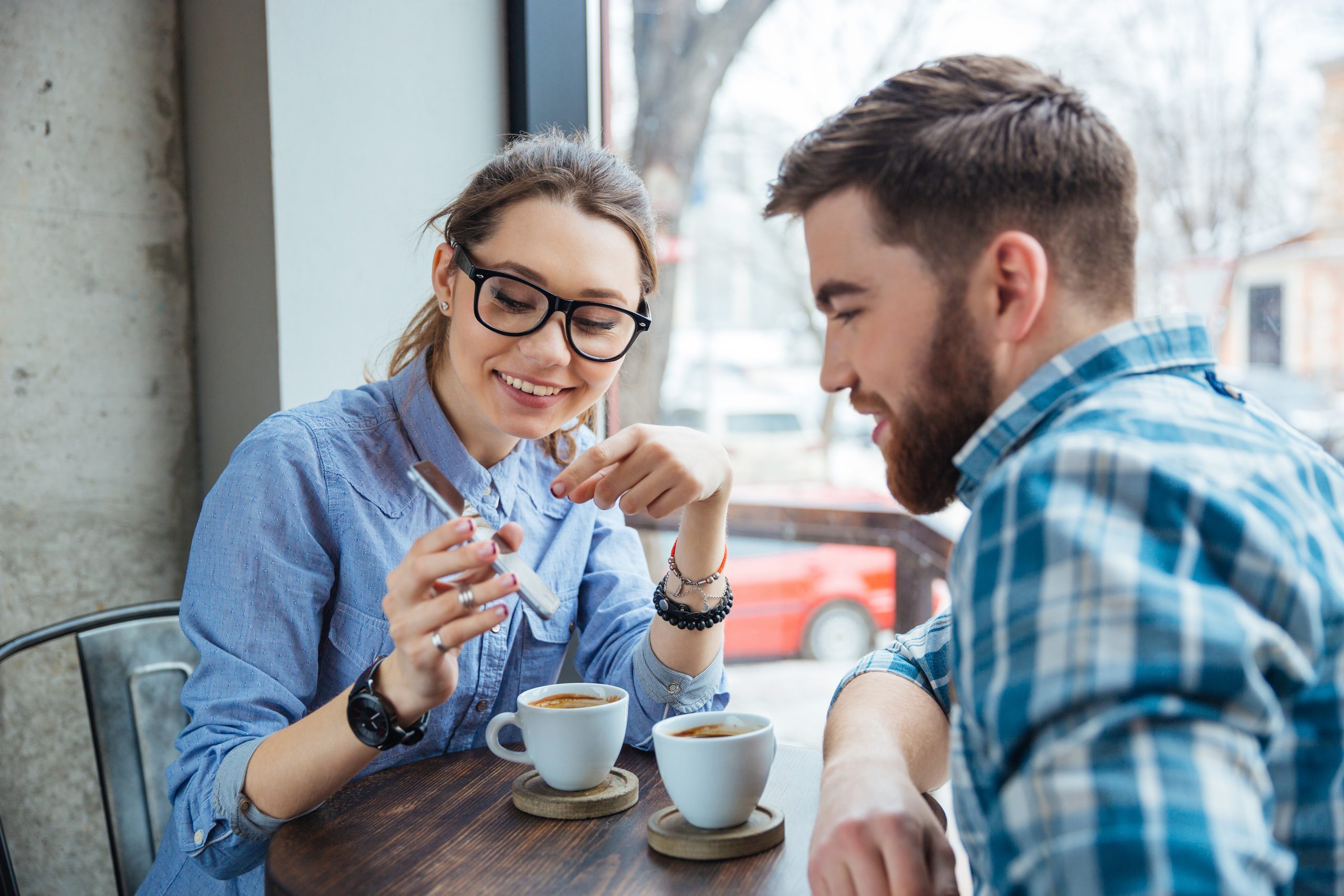woman showing man her phone over coffee